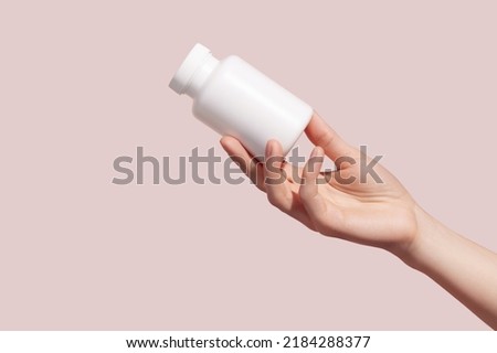 Female hand holding blank white squeeze bottle plastic tube on pink background. Packaging for pills, capsules or supplements. Mockup. High quality photo Royalty-Free Stock Photo #2184288377