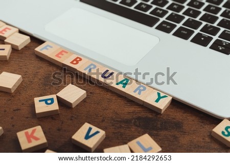 February - colourful wooden square letters on a dark wooden table next to a silver laptop with black keyboard. High quality photo