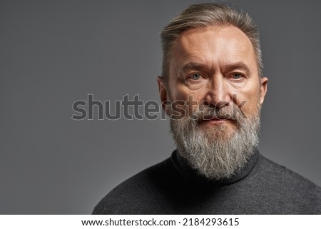 Portrait of serious senior caucasian man looking at camera. Stylish bearded pensioner wearing sweater. Concept of modern elderly male lifestyle. Isolated on grey background. Studio shoot. Copy space