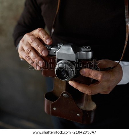 Cropped image of elderly man with old photo camera. Elegant bearded pensioner. Modern senior male lifestyle. Entertainment and hobby. Isolated on rusty concrete background. Studio shoot
