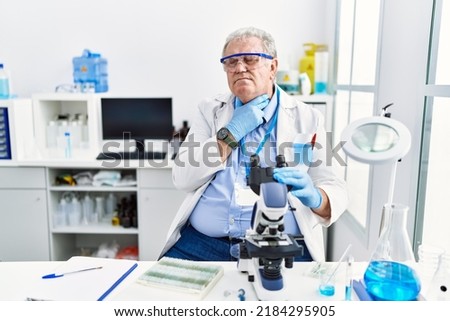 Senior caucasian man working at scientist laboratory touching painful neck, sore throat for flu, clod and infection 
