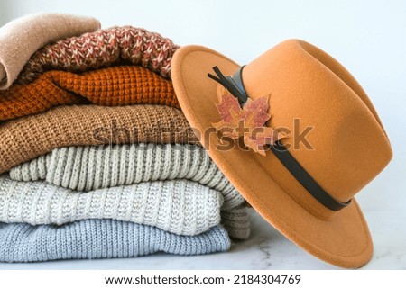 Stack of cozy knitted warm sweater with Autumn fall maple leaf and beige stylish hat. Sweaters in retro Style. Orange and blue colors. Cozy hygge concept Copy space Autumn season