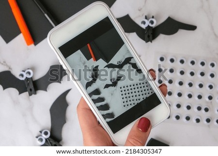 Taking photo on mobile phone of handmade Paper bats. Halloween holiday decorations. Happy Halloween party concept. Children's art project. DIY concept. Step by step Craft idea