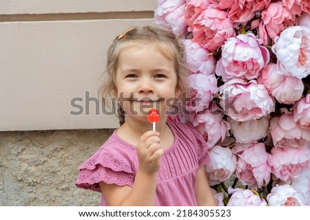 street portrait of a 4-year-old girl, holding a lollipop in her hands against the background of flowers in summer.