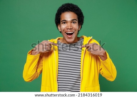 Confident cheerful happy blithesome young black curly man 20s years old wears yellow waterproof raincoat outerwear pointing thumb fingers on himself isolated on plain green background studio portrait