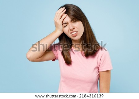 Young sad caucasian woman 20s wearing pink t-shirt put hand on face facepalm epic fail mistaken omg gesture isolated on pastel plain light blue background studio portrait. People lifestyle concept.