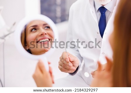 Woman looking in the mirror and smiling after checkup at dentist office; dentist and patient at dental clinic Royalty-Free Stock Photo #2184329297