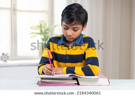 Indian boy student writing on notebook and doing his homework Royalty-Free Stock Photo #2184340065