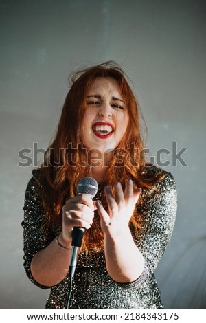 Portrait of redhead female singer woman in sparkly evening dress holding microphone