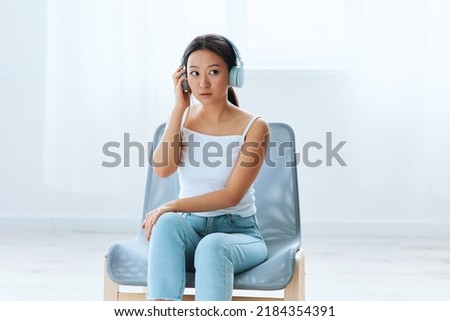 Excited shocked tanned lovely young Asian lady in headphones looks aside listens to external sounds at home interior living room. Sound Studio Stream Social media concept. Cool offer Banner Wide