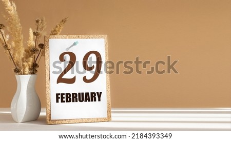 february 29. 29th day of month, calendar date.White vase with dead wood next to cork board with numbers. White-beige background with striped shadow. Concept of day of year, time planner, winter month.