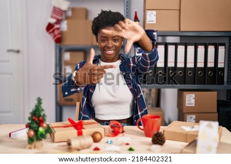 African american woman working at small business doing christmas decoration smiling making frame with hands and fingers with happy face. creativity and photography concept. 