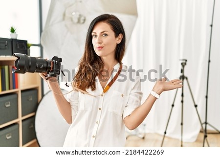 Beautiful caucasian woman working as photographer at photography studio smiling cheerful presenting and pointing with palm of hand looking at the camera. 