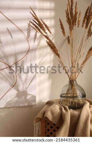 Vase with decorative dried plants and painting in stylish room interior