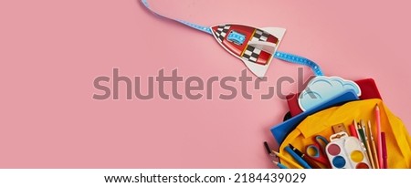 School backpack with colorful school supplies and rocket on pink background