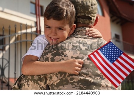 Soldier and his little son with flag of USA hugging outdoors