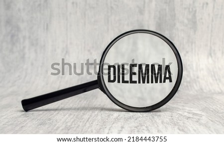 DILEMMA word on magnifier on wooden background