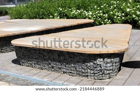 Wooden benches from gabion baskets with stones inside. Wood mounted on gabions. Benches of modern design. There is a recreation area. Detail of a low gabion wall with a wooden top Royalty-Free Stock Photo #2184446889
