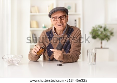 Smiling elderly man sitting at home and taking a pill from a bottle Royalty-Free Stock Photo #2184456325