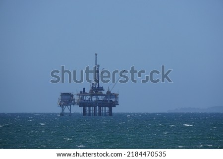 Offshore oil well in Santa Barbara, California is standing in the calm blue waters of the Pacific Ocean with the blue sky in the background.