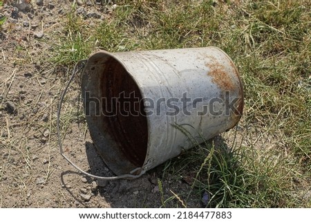 one old rusty empty metal bucket lies on the ground and green grass on the street Royalty-Free Stock Photo #2184477883