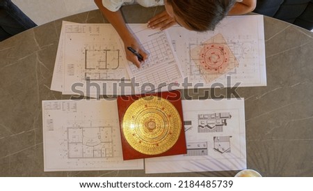 TOP DOWN: Young female analysing and making plan of feng shui for house building. Feng shui expert analysing energy flow distribution for balanced home and efficient house interior design arrangement. Royalty-Free Stock Photo #2184485739