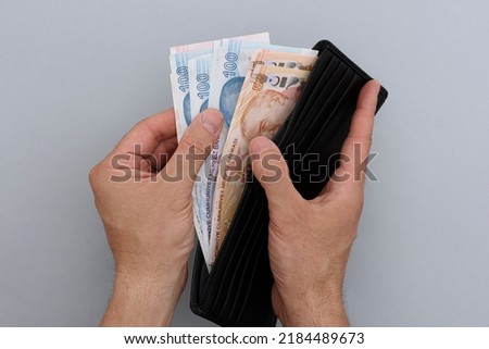 Male hand holding wallet with Turkish lira banknotes. Gray background. Royalty-Free Stock Photo #2184489673