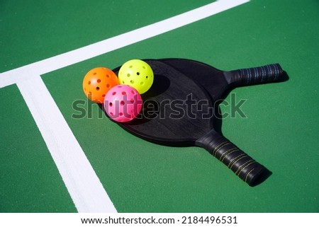 Two pickleball paddles and multiple pickle balls on court.                               Royalty-Free Stock Photo #2184496531