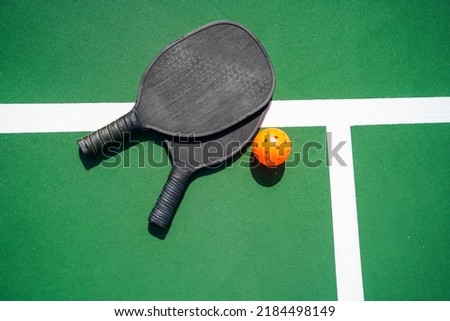 Two Pickleball Paddles and pickle ball on court.                                      Royalty-Free Stock Photo #2184498149