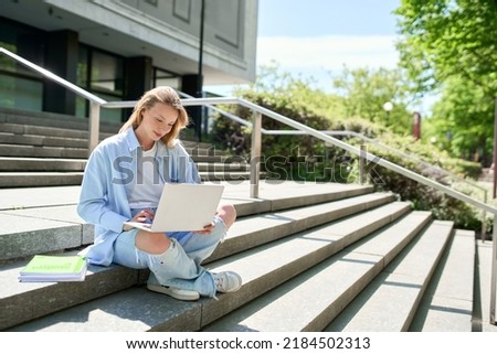 Smiling girl student using laptop computer modern technology device outdoor in university campus online learning, elearning outside sitting on urban stairs. Web education course webinars concept. Royalty-Free Stock Photo #2184502313