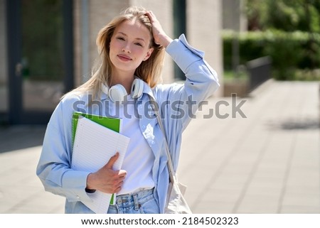 Pretty smiling girl university student holding notebooks looking at camera posing for outdoor portrait. College study programs, academic education ads, admission and scholarship. Royalty-Free Stock Photo #2184502323