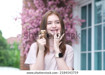 Outdoor closeup fashion photo of hipster caucasian girl holding  ice cream in summer hot weather with green garden colorful flower background  have fun and good mood.