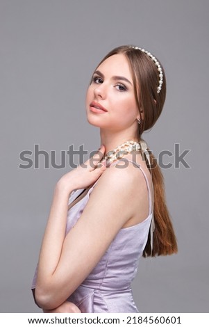 Stylish portrait of a beautiful girl with clean skin. Studio portrait of a young girl with a diadem and pearl necklace on a gray background. place for advertising