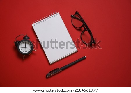 Alarm clock glasses notepad pen on table, red background, text space, selective focus, education and business deadline concept