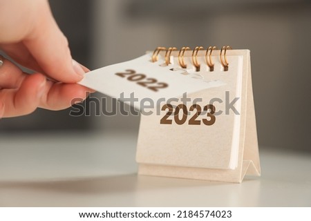 a woman's hand turns over a calendar sheet. year change from 2022 to 2023. Royalty-Free Stock Photo #2184574023