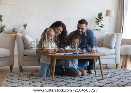 Mother and father helping little sibling children to draw in colored pencils, enjoying creative hobby, leisure time together, sitting on warm carpeted heating floor. Family home activities concept