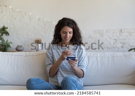 Happy beautiful Hispanic customer woman holding credit card, using online shopping app on smartphone, making payment on Internet store website, paying bills, fees, inserting data