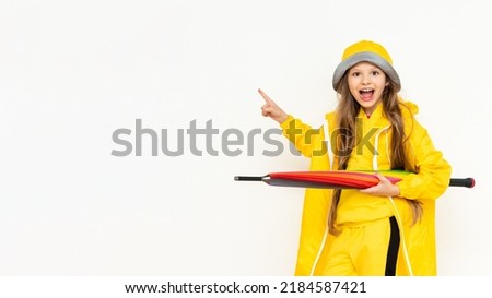 The child holds the umbrella horizontally, smiling broadly and pointing at your advertisement. A little girl in a yellow raincoat and a panama hat on a white isolated background. Copy Space.