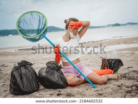 A female ecologist volunteer is resting after cleaning the beach on the seashore from plastic and other waste