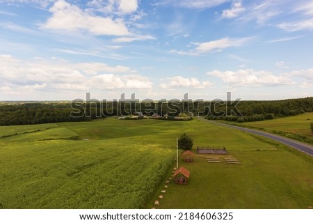 wide horizontal nature view with green grass, wooden houses, green forest and blue sky