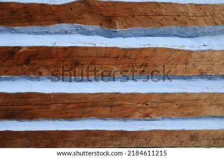 The wall of a wooden house, the spaces between the logs of wood having been filled with clay and painted