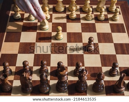 Woman's hand moving chess piece on wooden board and pieces. Concept woman in chess and sport