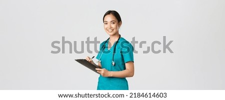 Healthcare workers, preventing virus, quarantine campaign concept. Smiling friendly female doctor, nurse in scrubs writing dorn results analysis at clipboard, standing white background