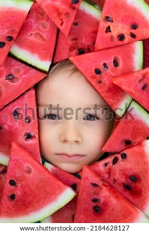 The face of a child in a frame of watermelon slices.Red berry pulp.A boy framed by triangular pieces of watermelon.Funny summer picture.Cute portrait of a baby.