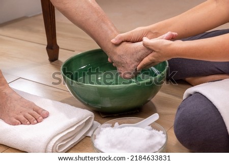 Female caregiver wipes the elderly woman feet by towel.