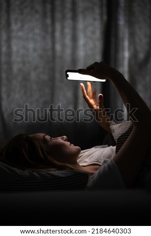 Young woman in bed holding a phone, tired and exhausted, blue light straining her eyes, messing up her circadian rhytm Royalty-Free Stock Photo #2184640303