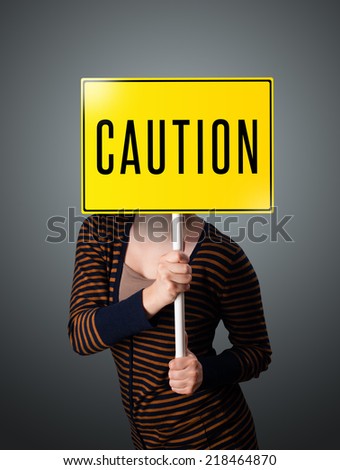 Young lady standing and holding a yellow caution sign in front of her head