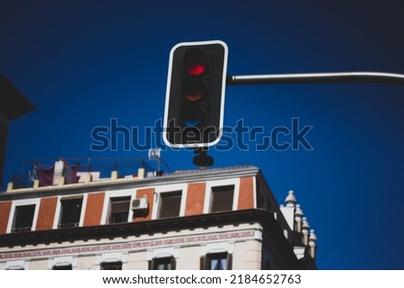Red traffic light against a background of blue gloomy sky and residential buildings. Urban infrastructure. Regulation of vehicular traffic, traffic on the street. Semaphore lights. Stop and wait sign. Royalty-Free Stock Photo #2184652763