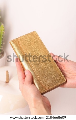 golden leather purse folder in hands close up photo on white wall background 