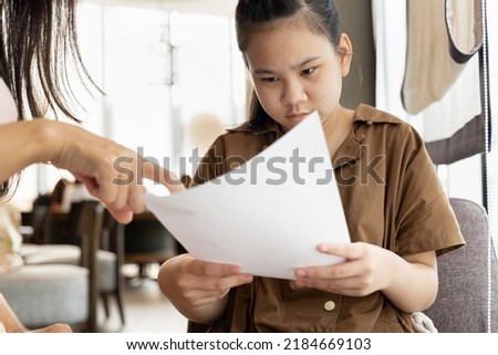Asian mother hand pointing at poor grading from examination result report of her daughter Royalty-Free Stock Photo #2184669103